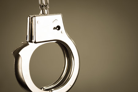 Closeup shot of metallic handcuffs over grey background color toned