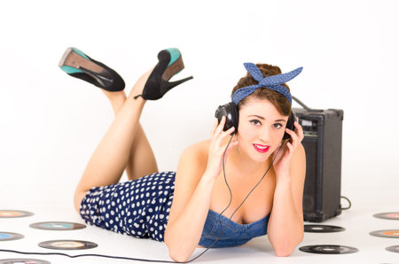 Beautiful young girl listening to headphones in retro clothes and hairstyle representing pinup style...
