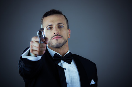 Handsome young man gangster police spy agent assissin holding and pointing a gun wearing a suitの写真素材