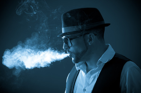 Young handsome stylish bohemian musician male model wearing sunglasses and hat smoking a cigarette color tonedの写真素材