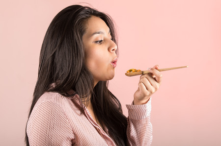 young girl eating vegetables and rice from a wooden spoon side portraitの写真素材