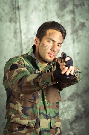 portrait of soldier militar latin man in camouflage uniform pointing a gun to the frontの写真素材