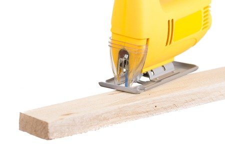 yellow electric jigsaw cutting plank of wood isolated on whiteの写真素材