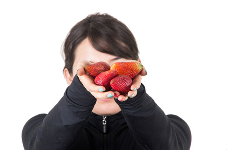 closeup portrait of young girl holding offering red strawberries isolated on whiteの写真素材