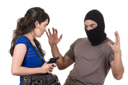 beautiful girl pointing gun at surprised masked male thief isolated on white