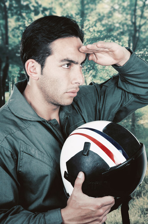 young handsome proud pilot wearing uniform and holding helmet saluting outdoors backgroundの写真素材
