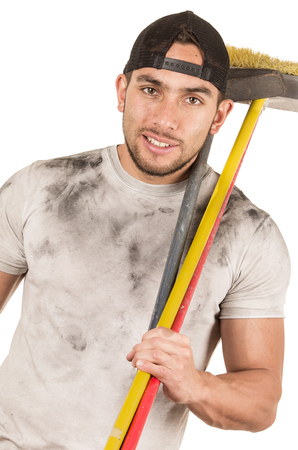 happy young muscular latin construction worker cleaner holding broom isolated on whiteの写真素材