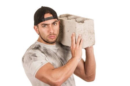 young muscular latin construction worker carrying a brick isolated on whiteの写真素材