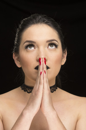 young gothic beautiful woman with black makeup and red nails prayingの写真素材