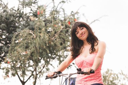 beautiful young brunette girl riding bicycle in the park low angle viewの写真素材