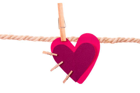 pink heart with small clothespins attached hanging on a rope clothesline isolated on whiteの写真素材