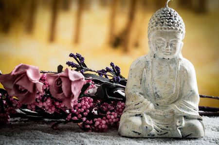 closeup of small sculpture of buddha over white pebbles with pink flowers in the backgroundの写真素材