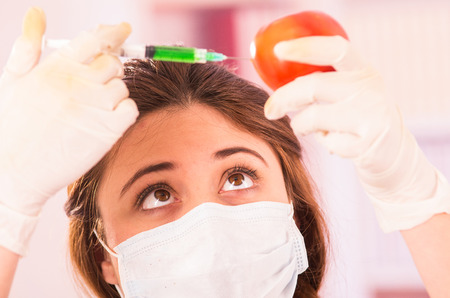 young female biologist injecting a syringe in a tomato concept of genetically modified foodの写真素材