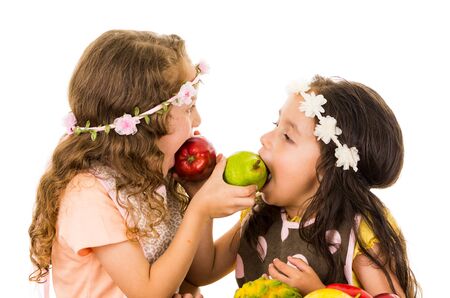 Beautiful healthy little girls feeding each other delicious fresh fruits isolated on whiteの写真素材