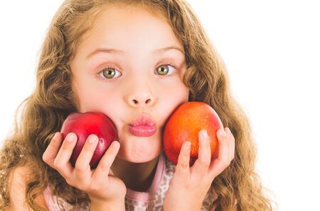 Cute little preschooler girl holding two peaches in front of her cheeks isolated on whiteの写真素材