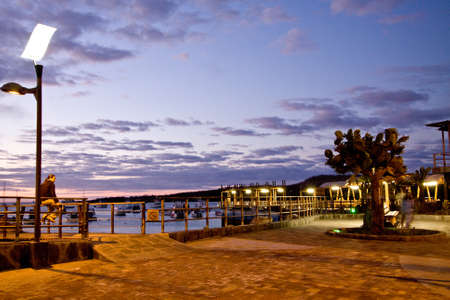 GALAPAGOS, ECUADOR - JULY 27, 2010: Unidentified tourist admiring magical sunset along the port in San Cristobal island, Galapagosのeditorial素材