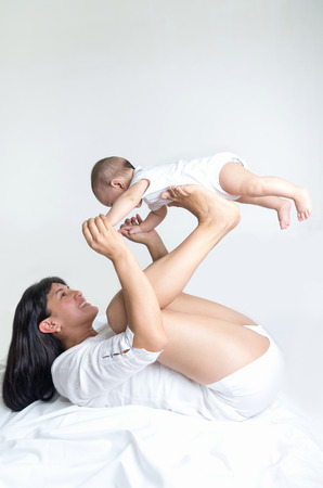 Beautiful mother playfully holding baby with her hands and legs isolated on whiteの写真素材