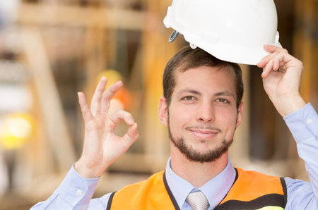 young handsome smiling architect supervising a construction saluting with helmet