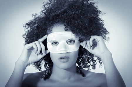 young woman with short curly dark hair wearing a white mask isolated on white vignette background, color tonedの写真素材