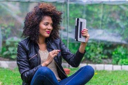 exotic beautiful young girl with dark curly hair sitting in the using tablet