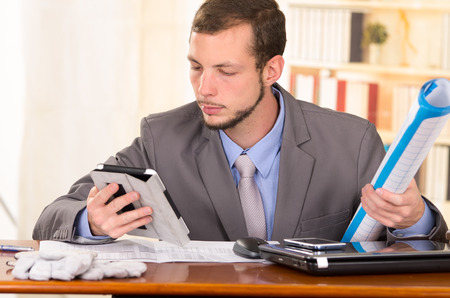 young handsome busy architect sitting in front of his desk working using tabletの写真素材