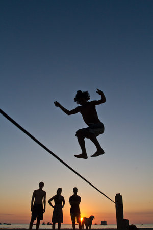 Silhouette of young man balancing jumping on slackline during sunset at a beach in Manabi, Ecuador