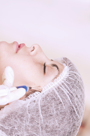 Close up portrait of girl getting injection in face, concept of cosmetic treatmentの写真素材