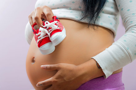 caption of pregnant belly and hands holding up baby converse shoesの写真素材