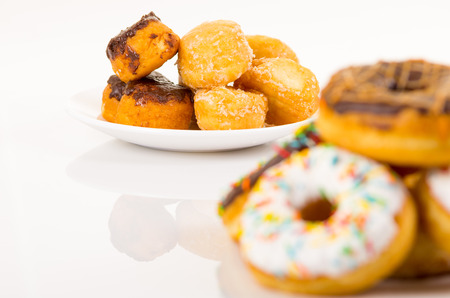 traditional donuts of chocolate and vanilla in front slightly out of focus and another plate of covered donuts in backgroundの写真素材