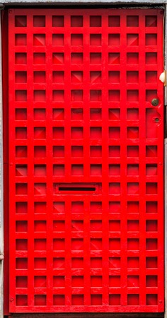 Strong red door with artsy metal gate in front forming a pattern of small squaresの写真素材