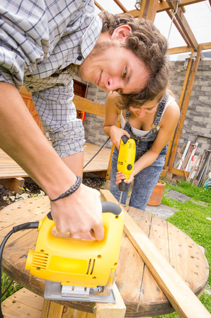 Couple working together on renovation project outdoors using a jigsaw and power drill.の写真素材