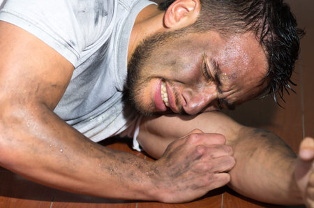 Closeup hispanic man with dirty face and shirt on floor locking burying head inside left arm as in...