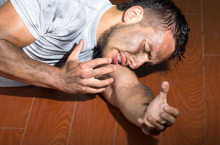 Hispanic man with dirty face and shirt lying on floor left arm reaching towards camera.の写真素材