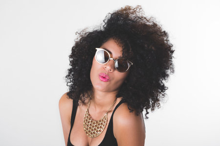 Headshot hispanic model wearing black dress, golden necklace, sunglasses and curly hair making kiss...