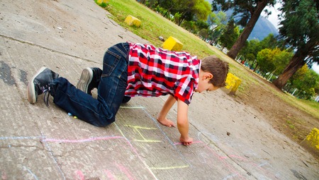 Elegant boy drawing hopscotch with chalk on the groundの写真素材