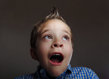 Low key portrait of cute boy looking surprised over gray background