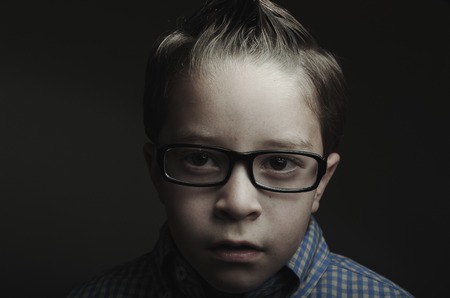 Low key closeup portrait of little boy wearing glasses looking sadの写真素材