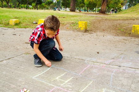 Elegant boy drawing hopscotch with chalk on the groundの写真素材