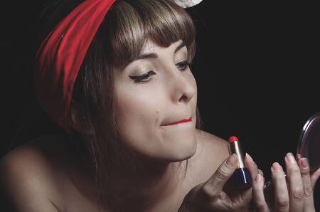 Closeup portrait of cute young girl putting red lipstick onの写真素材