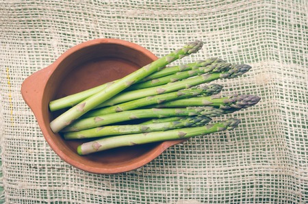 Fresh bunch of green asparagus in ceramic terracota bowl on a hemp cloth.の写真素材