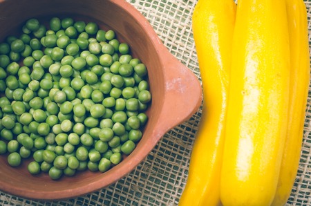 ceramic terracota bowl of fresh organic green peas next to exquisite yellow zucchinis.の写真素材