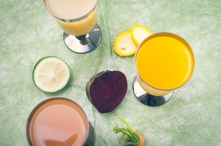 organic delicious cups of orange juice placed on table next to lime, zucchini, beetroot and carrot.の写真素材