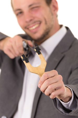 Handsome buisness man smiling concentrated aiming a slingshot isolated over white background.の写真素材