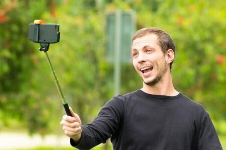 Hispanic man posing with selfie stick in park environment smiling happily.の写真素材