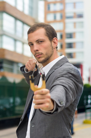 Handsome buisness man concentrated aiming a slingshot at urban city background.の写真素材