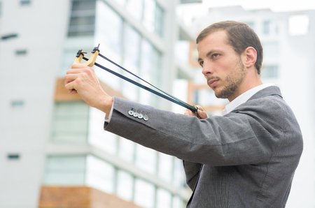 Handsome buisness man concentrated aiming a slingshot at urban city background.の写真素材