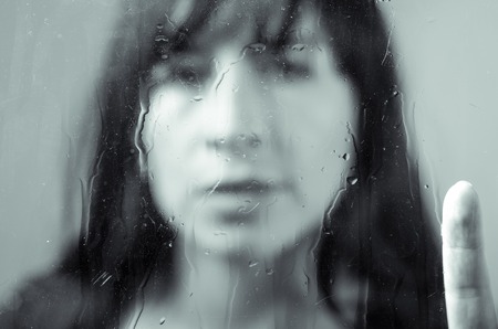 Black and white closeup diffused portrait of brunette girl behind glass concept of melancholy, sadness, lonelinessの写真素材