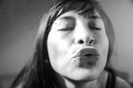 Black and white closeup portrait of brunette girl behind glass giving a kissの写真素材