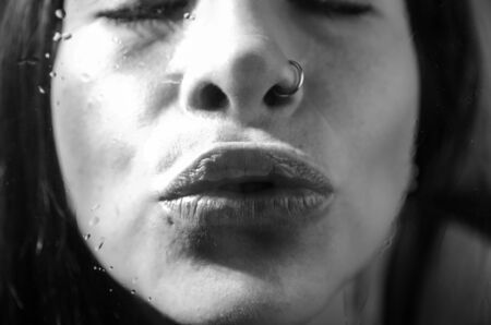 Black and white closeup portrait of brunette girl behind glass giving a kissの写真素材