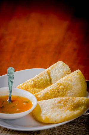 Three empanadas nicely arranged on white platter next to small salsa bowl and rustic background .の写真素材